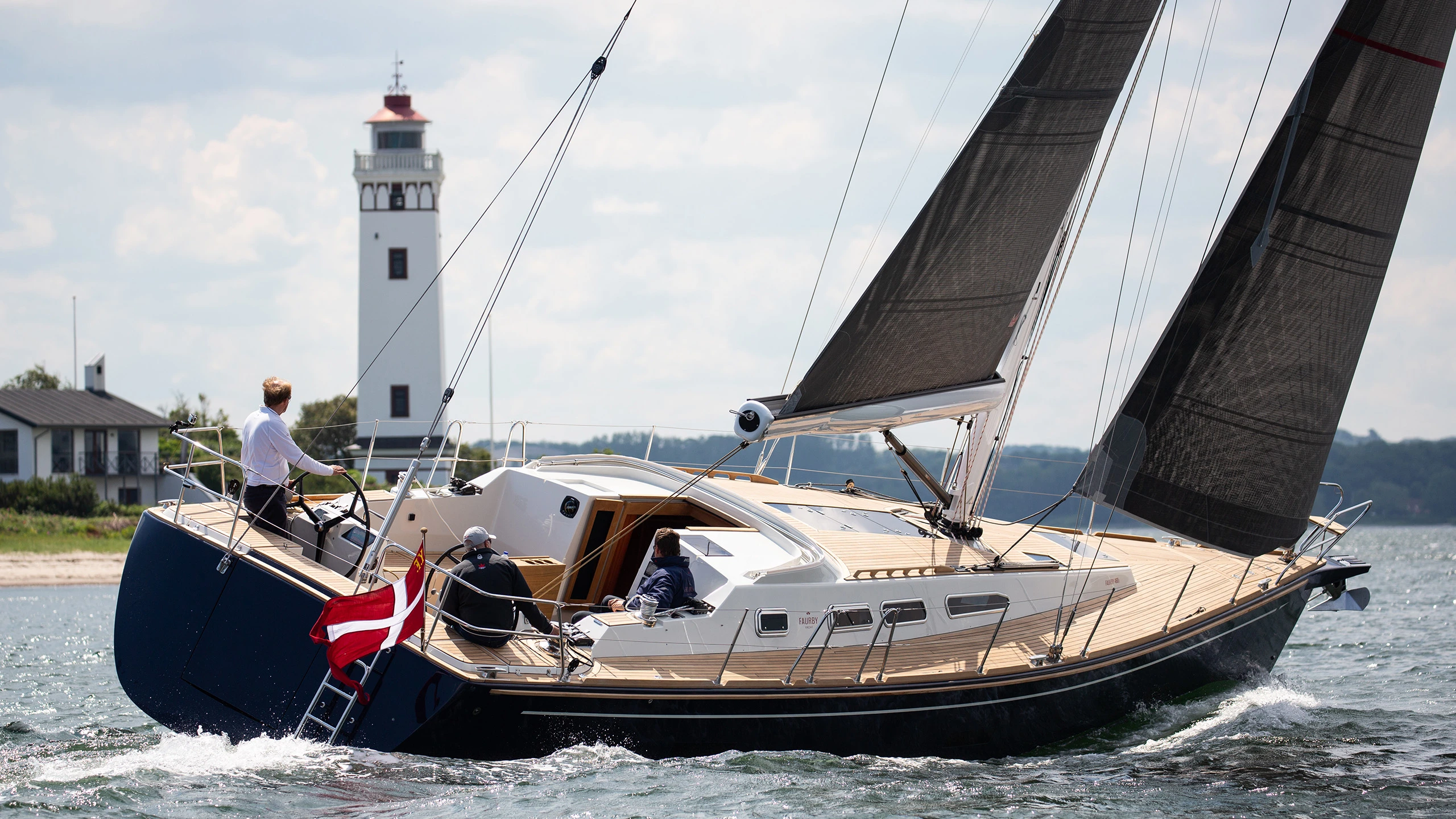 Faurby 460 with a blue hull and dark sails, sailing in front of a lighthouse