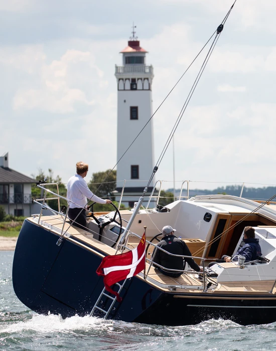 Faurby 460 with a blue hull and dark sails, sailing in front of a lighthouse