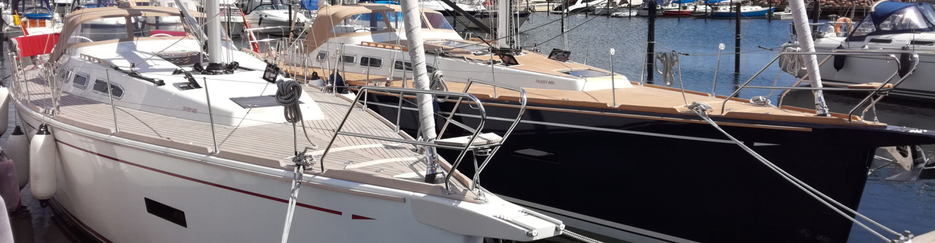 Faurby 460 with a blue hull and dark sails, sailing in front of a lighthouse
